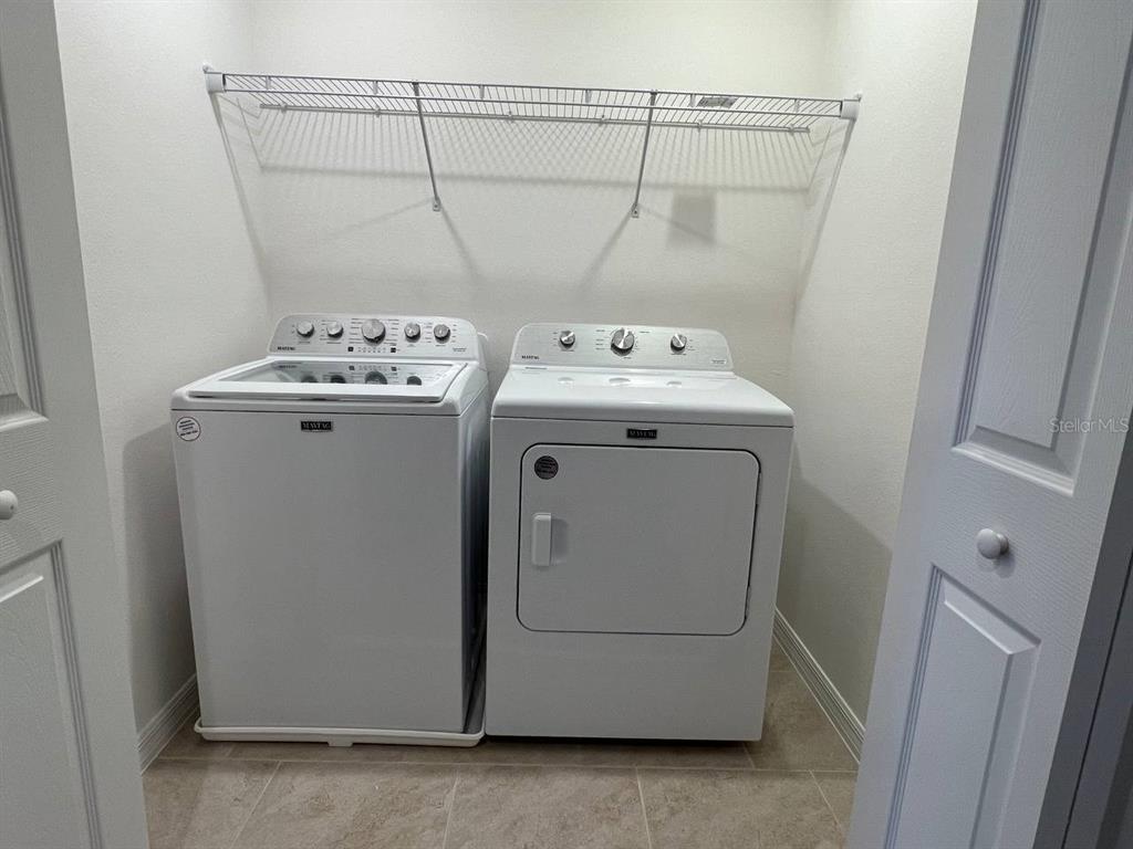 A laundry closet contains a white Maytag washer and dryer beneath a wire shelf — 1248 WISPY CYPRESS DRIVE, KISSIMMEE, FL