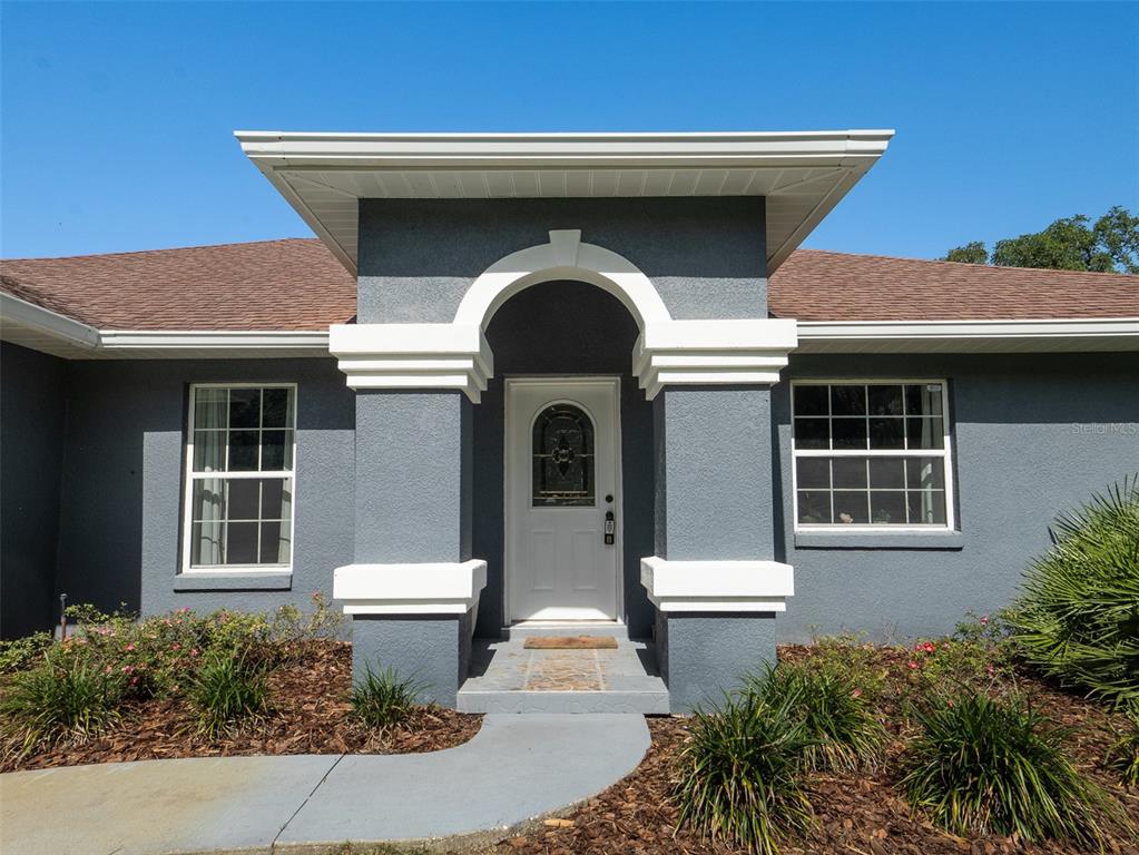 The exterior of a gray house features a white arched entryway and two windows — 8548 NW 115TH AVENUE, OCALA, FL