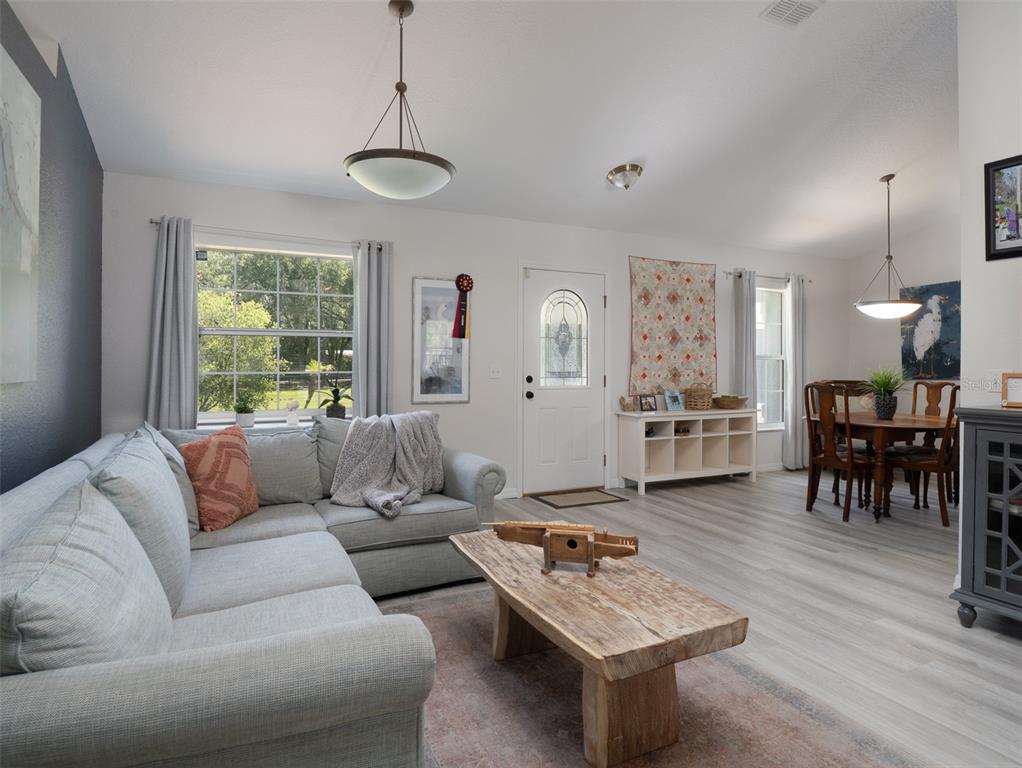 A living room with light gray flooring, a sectional sofa, and an adjacent dining area — 8548 NW 115TH AVENUE, OCALA, FL