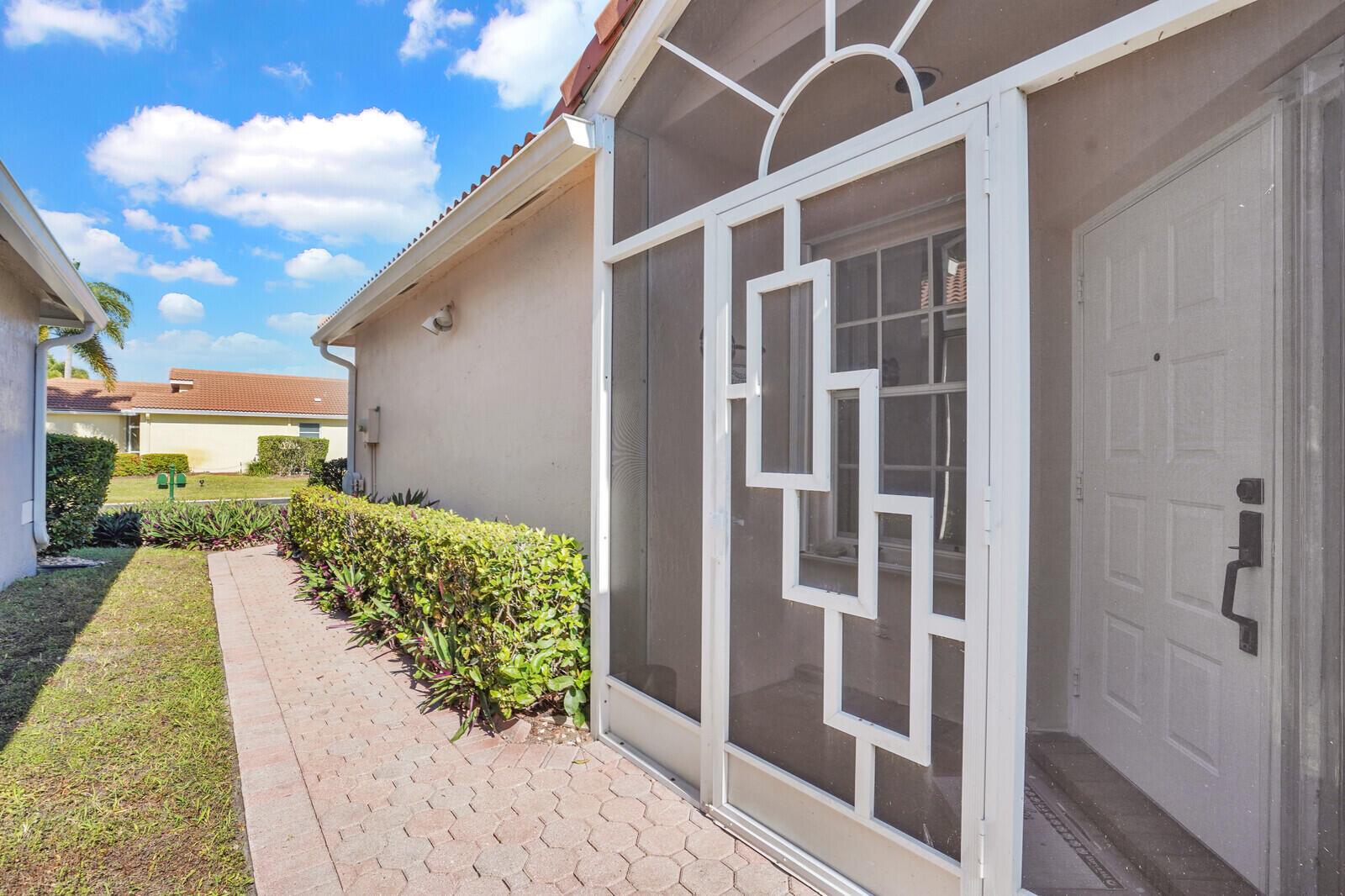 A white screen door leads to a front entrance with a brick walkway and hedges — 7756 Cherry Blossom Way, Boynton Beach FL 33437, BOYNTON BEACH, FL
