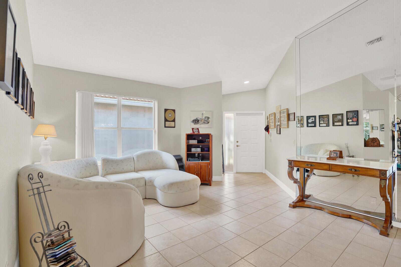 A living room features a white curved sofa, tile flooring, and a large wall mirror — 7756 Cherry Blossom Way, Boynton Beach FL 33437, BOYNTON BEACH, FL