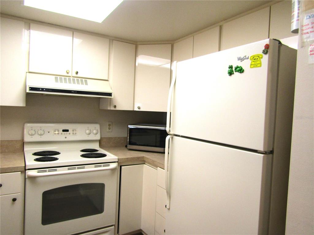 A kitchen features white cabinets, a white stove, a white refrigerator, and a microwave — 4632 RINGWOOD MEADOW UNIT 28, SARASOTA, FL
