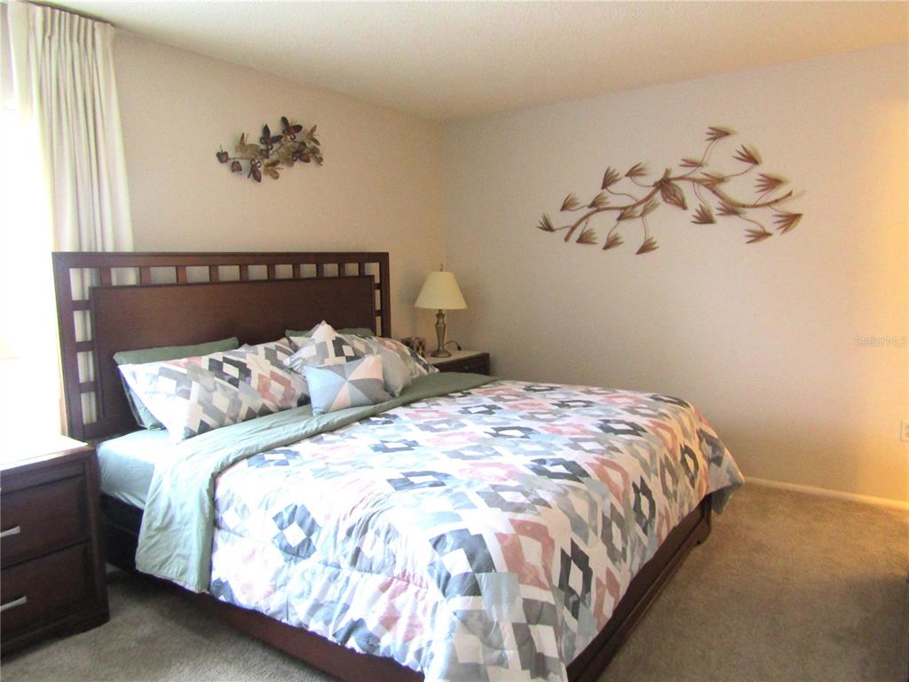 A bedroom features a wooden headboard, a patterned quilt, and metal wall art — 4632 RINGWOOD MEADOW UNIT 28, SARASOTA, FL