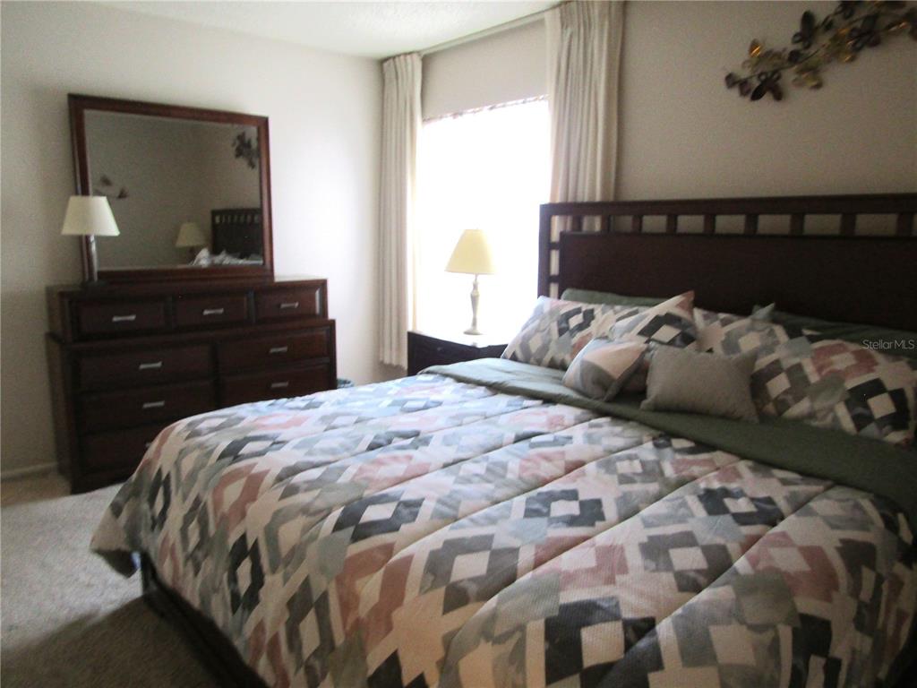 A bedroom features a wooden bed frame, a patterned comforter, and a matching dresser with mirror — 4632 RINGWOOD MEADOW UNIT 28, SARASOTA, FL