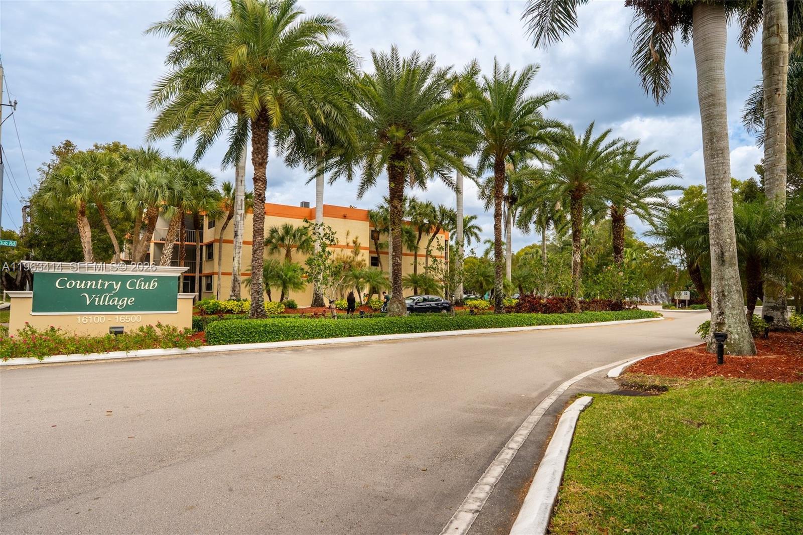 A green sign for Country Club Village stands before a multi-story building and palm trees — 16475 Golf Club Rd # 307, Weston FL 33326, WESTON, FL