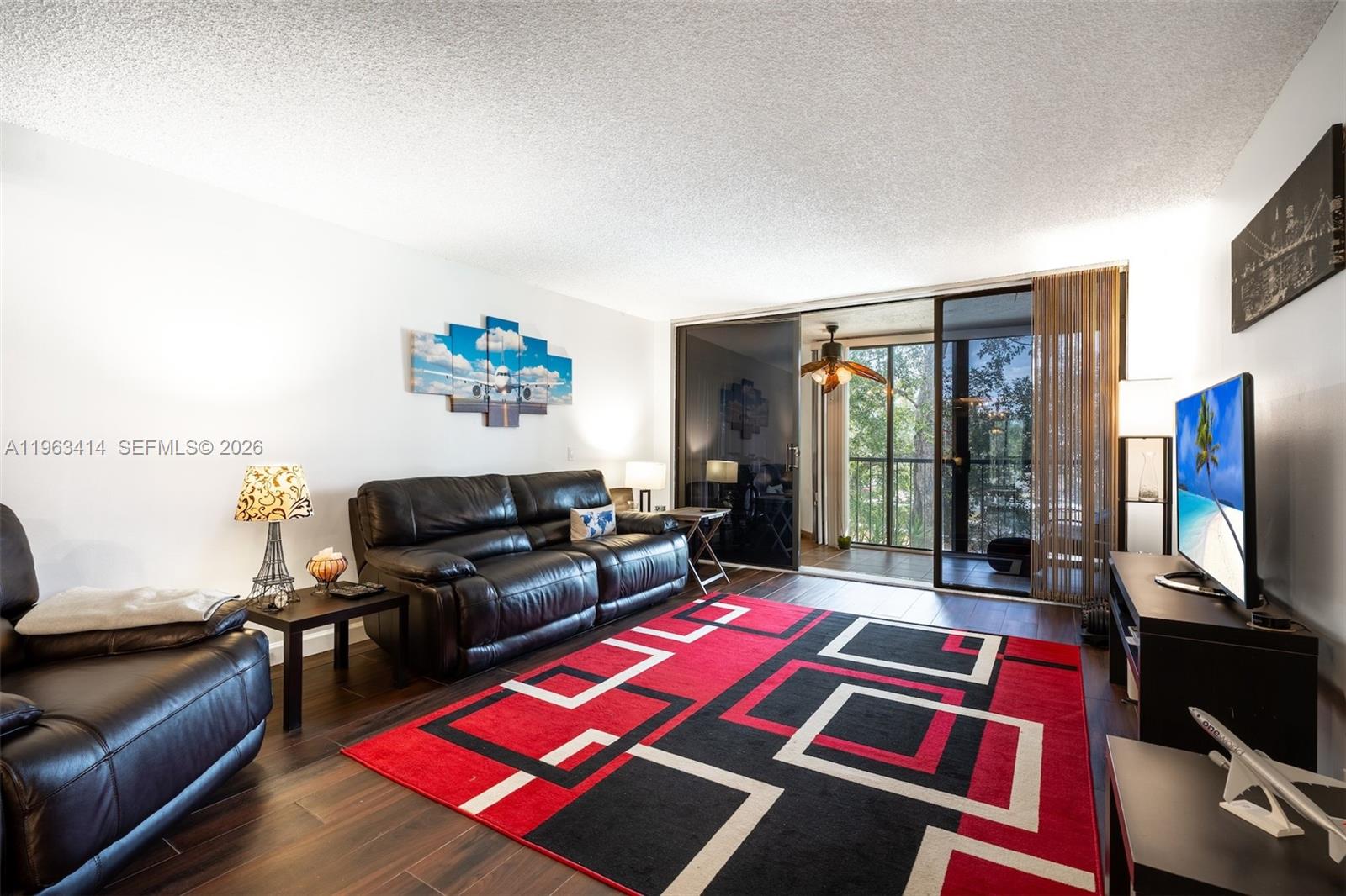 A living room features a black leather sofa, a geometric rug, and a sliding glass door — 16475 Golf Club Rd # 307, Weston FL 33326, WESTON, FL