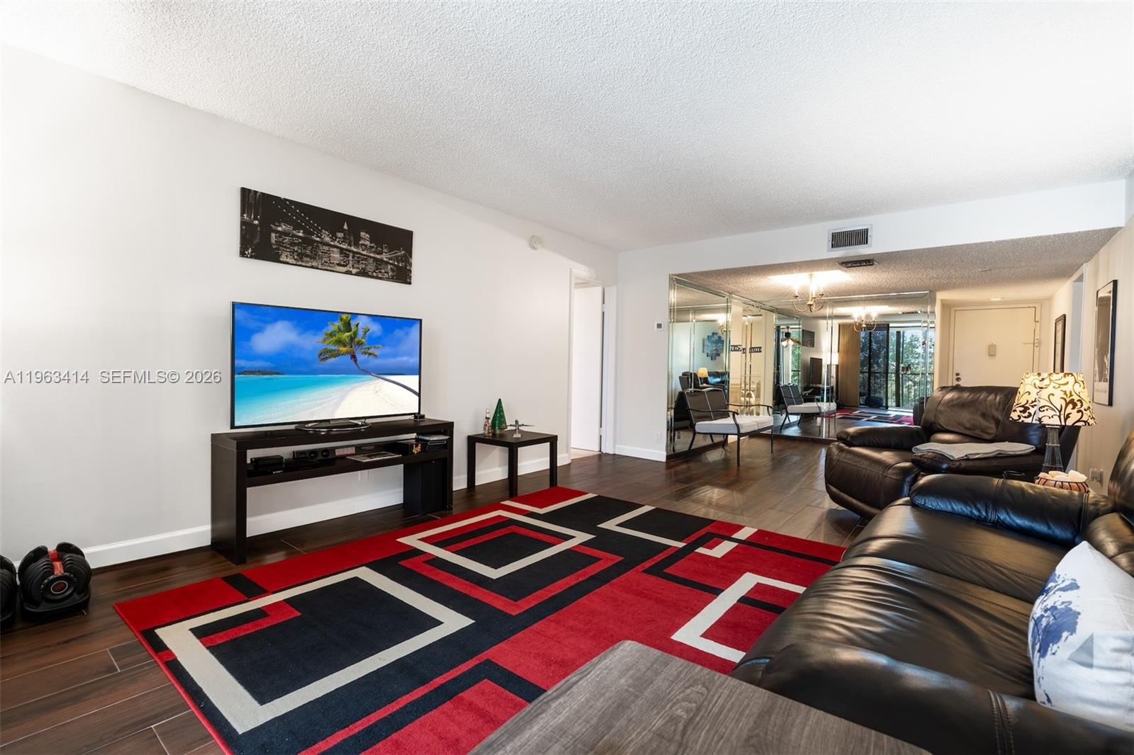 A living room features a red and black area rug, leather sofa, and mirrored wall — 16475 Golf Club Rd # 307, Weston FL 33326, WESTON, FL