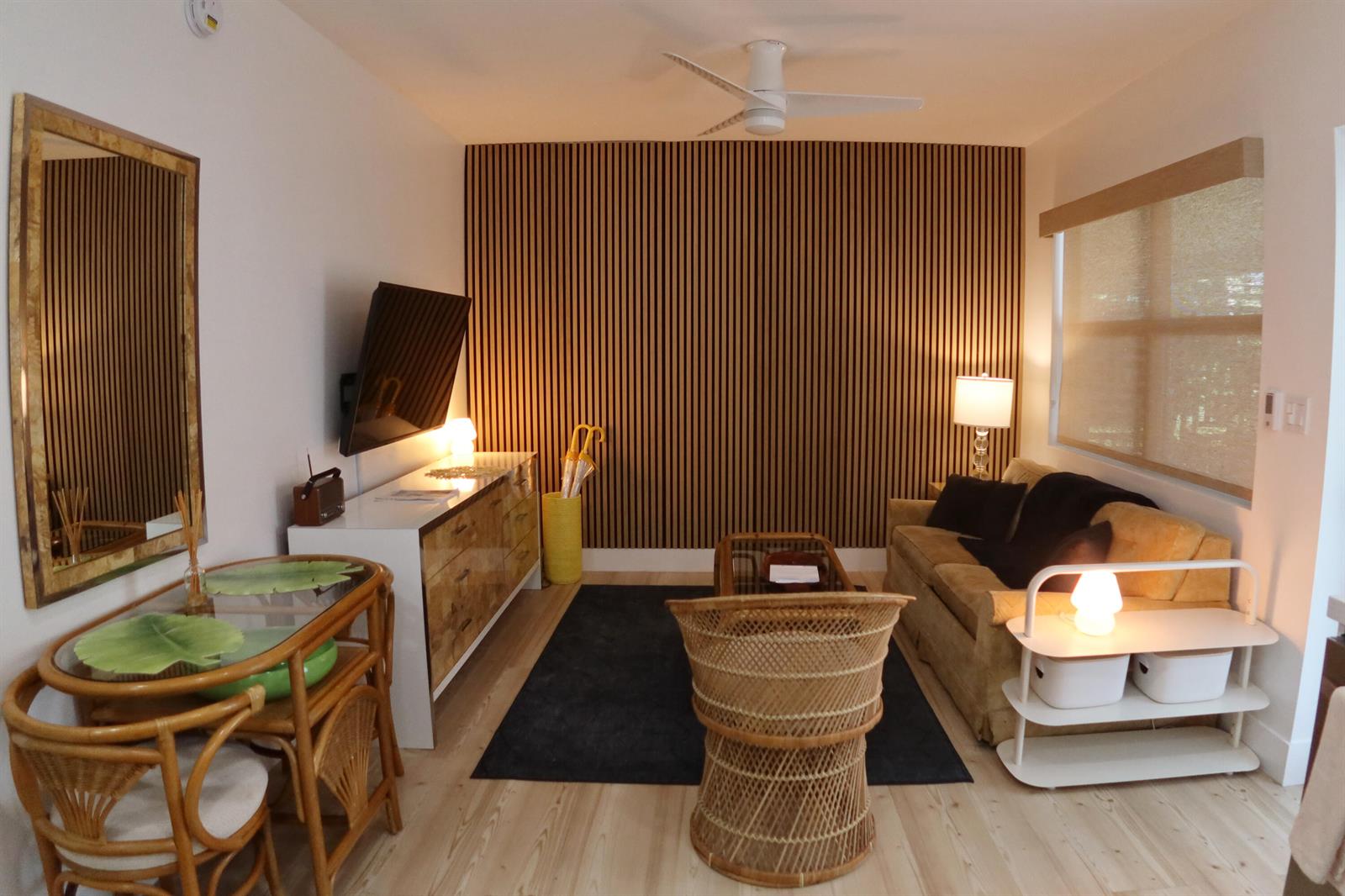 A living room features a slatted wood accent wall, a sofa, wicker chairs, and furniture — 3408 Spring Street # 2, Pompano Beach FL 33062, POMPANO BEACH, FL