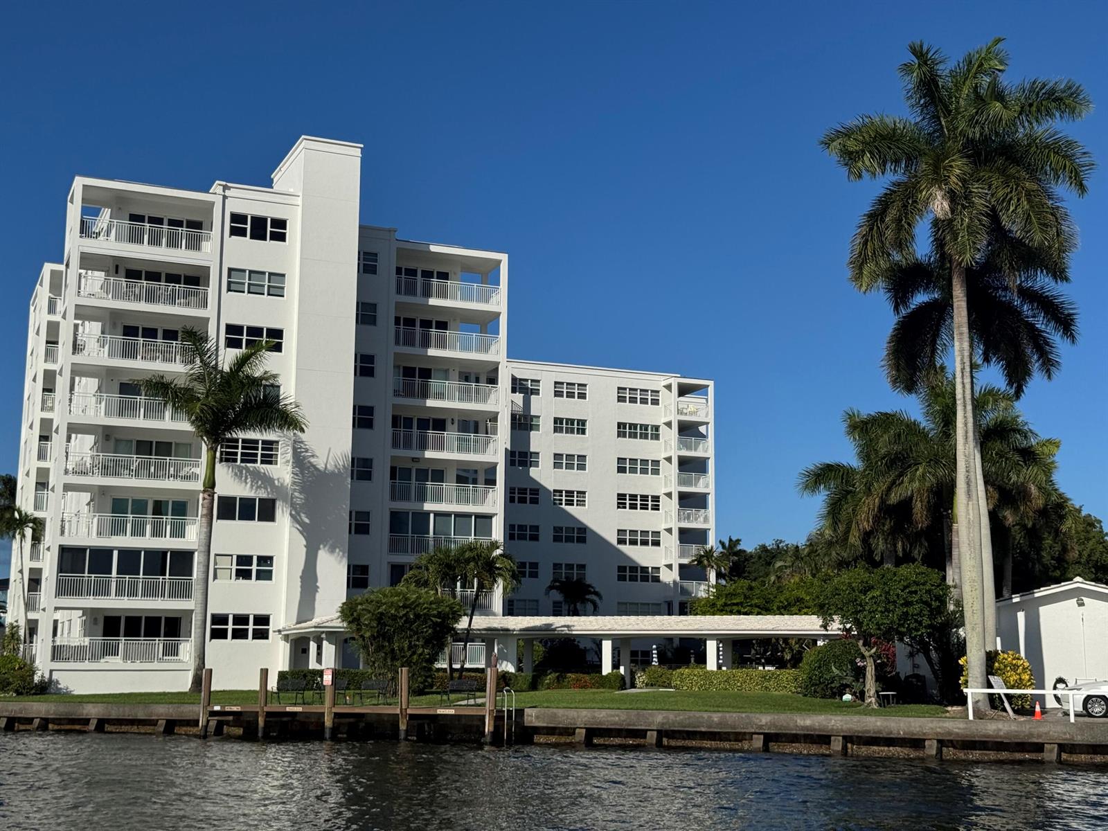 A white multi-story apartment building stands beside a canal with palm trees and a dock — 1000 Lowry Street # 3e, Delray Beach FL 33483, DELRAY BEACH, FL