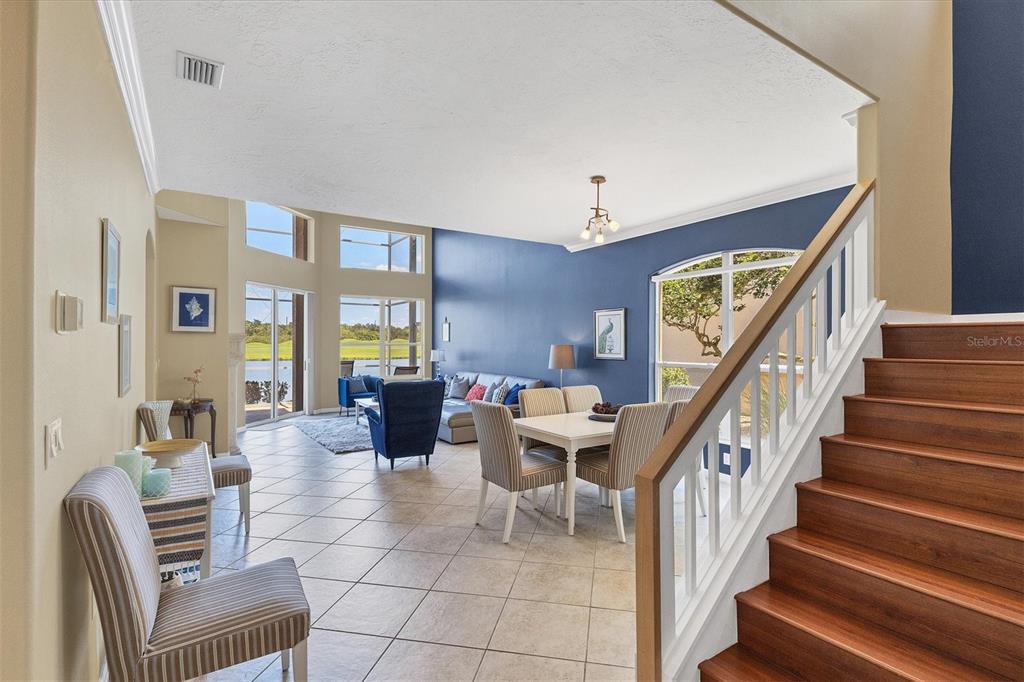 A living and dining area with tile floors, blue accent walls, and a wooden staircase — 7263 REGINA ROYALE UNIT 3, SARASOTA, FL