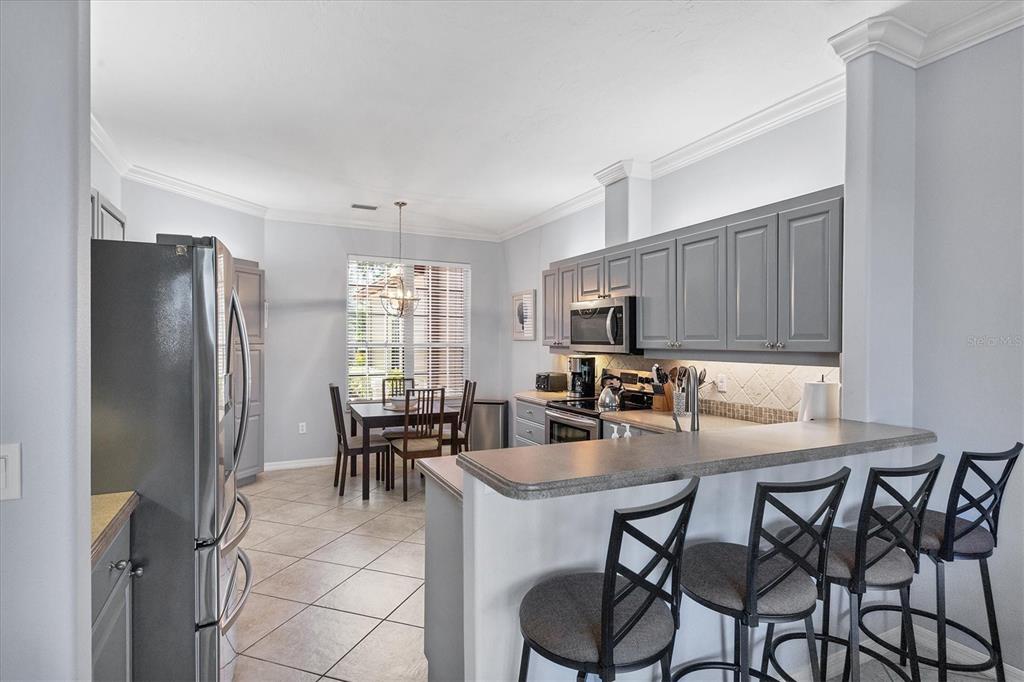 A kitchen features gray cabinets, stainless steel appliances, a breakfast bar, and an adjacent dining area — 7263 REGINA ROYALE UNIT 3, SARASOTA, FL