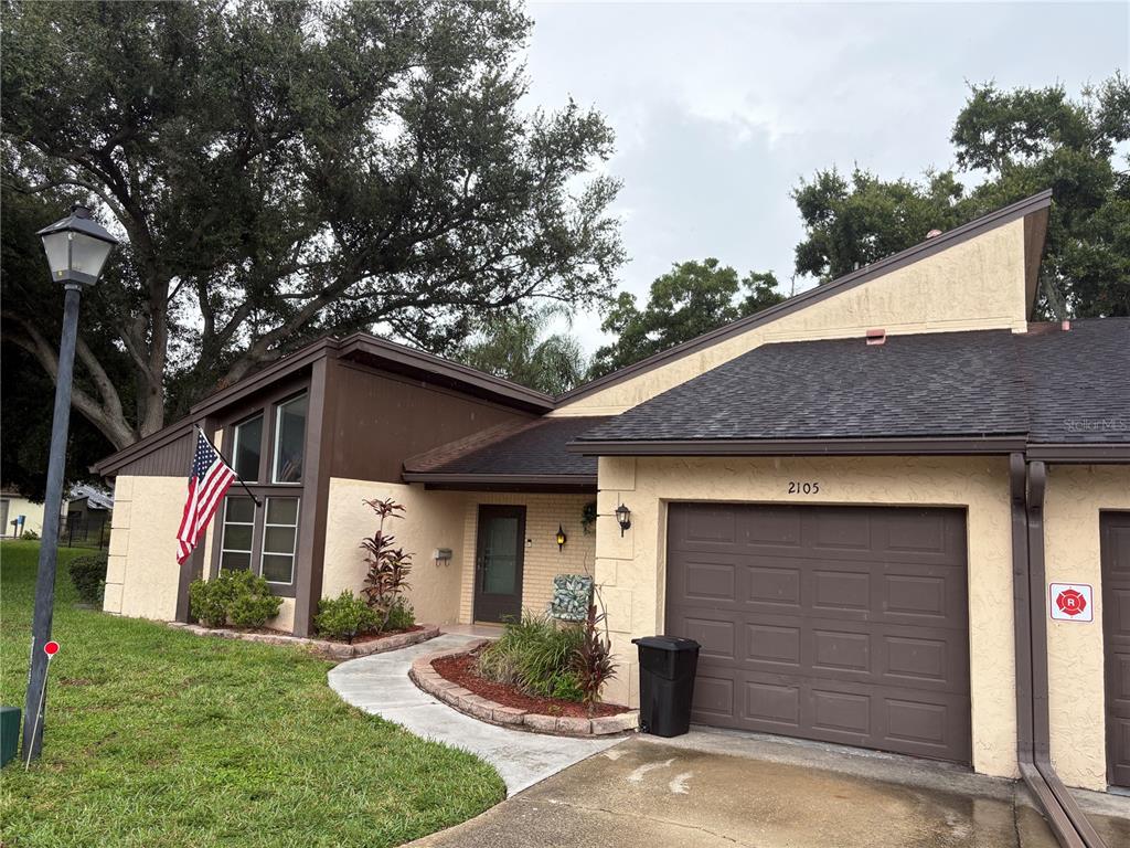 A single-story house with a brown garage, tan stucco walls, and a front walkway — 2101 SUNSET POINT ROAD UNIT 2105, CLEARWATER, FL