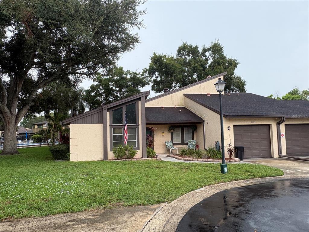 A tan single-story townhouse with a dark roof, garage, and a large tree in front — 2101 SUNSET POINT ROAD UNIT 2105, CLEARWATER, FL