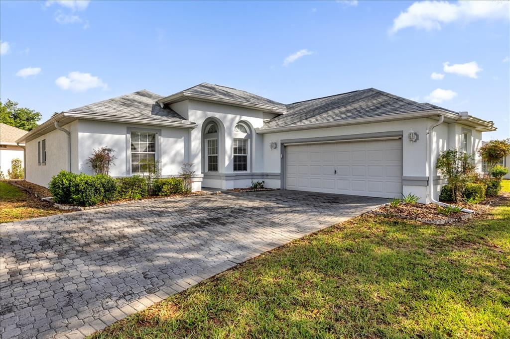A single-story house with a white stucco exterior, a gray shingled roof, and a paver driveway — 6359 SW 117TH LOOP, OCALA, FL