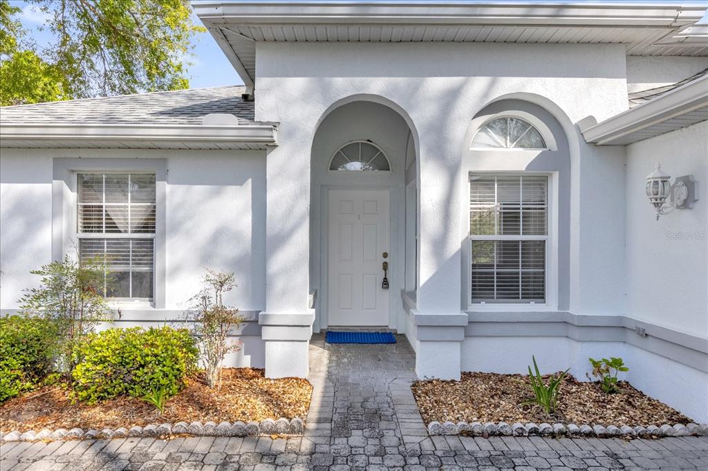 The exterior of a white house features an arched entryway, a white door, and windows — 6359 SW 117TH LOOP, OCALA, FL