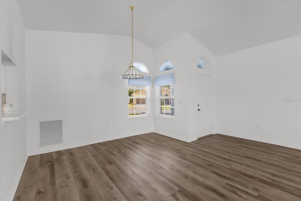 An empty room with white walls, vaulted ceilings, wood-look flooring, and a hanging light fixture — 6359 SW 117TH LOOP, OCALA, FL