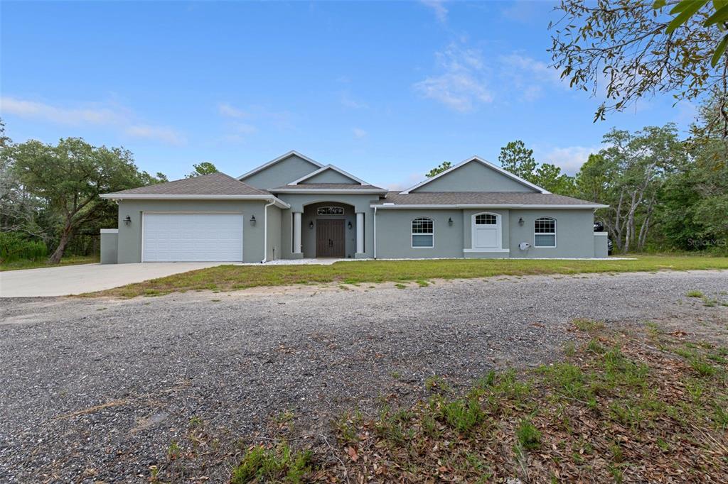A single-story house with a gray stucco exterior, a two-car garage, and a gravel driveway — 14610 HIDDEN DEER TRAIL, BROOKSVILLE, FL