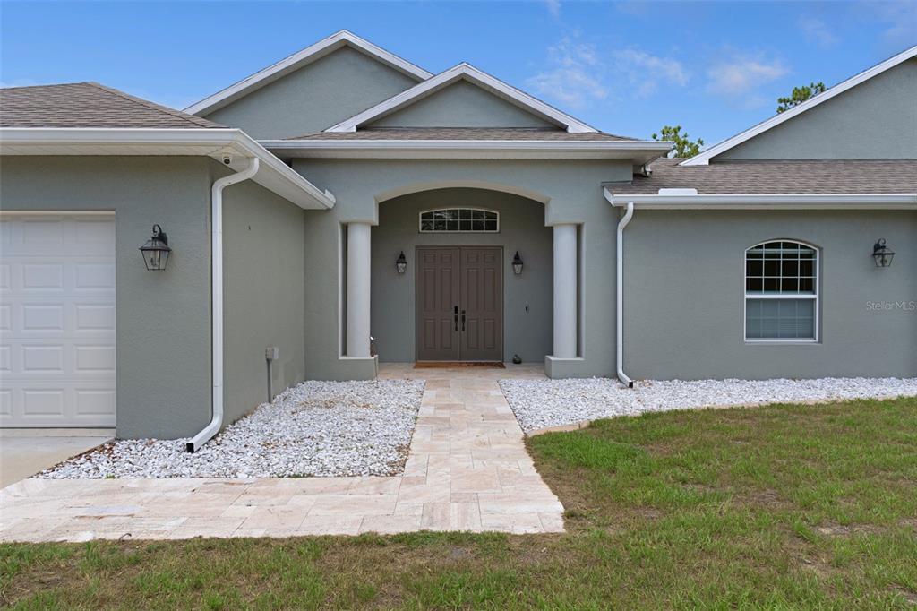 The exterior of a single-story house features a gray stucco facade, double front doors, and a stone walkway — 14610 HIDDEN DEER TRAIL, BROOKSVILLE, FL