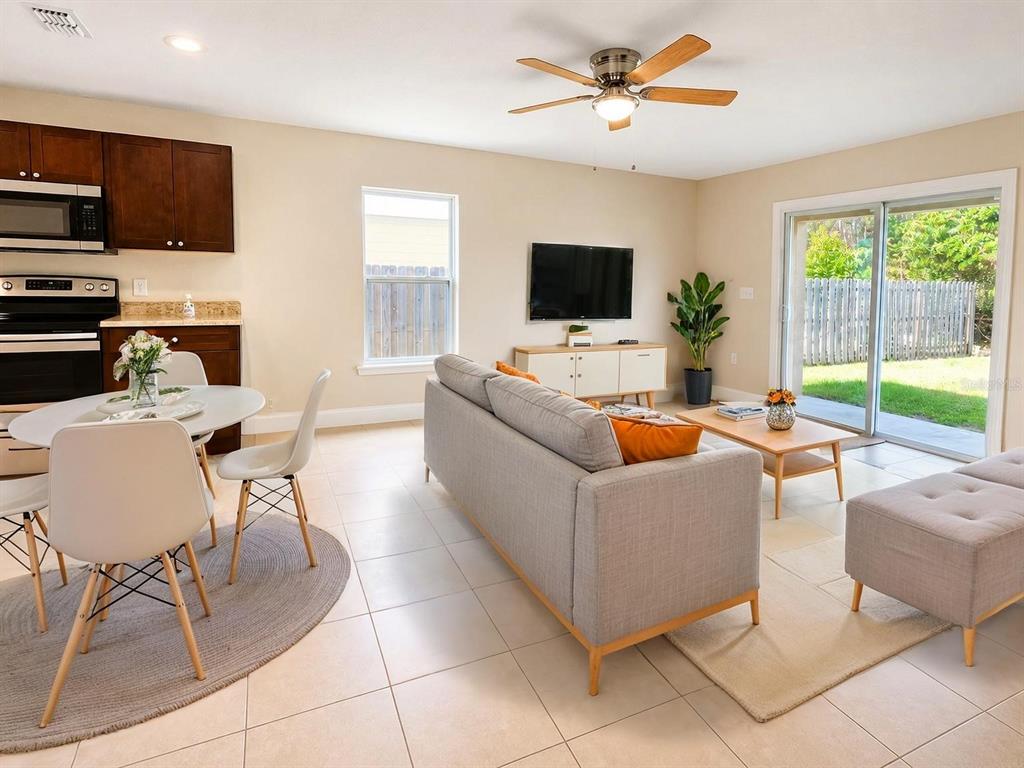 A living room and dining area with tile floors, a grey sofa, and sliding glass doors — 642 HERALDO COURT UNIT B, KISSIMMEE, FL