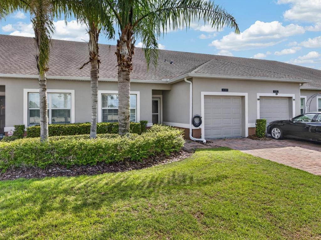 The exterior of a single-story attached home features a paved driveway, garage, and palm trees — 3530 FAIRWATERS COURT UNIT D, CLERMONT, FL