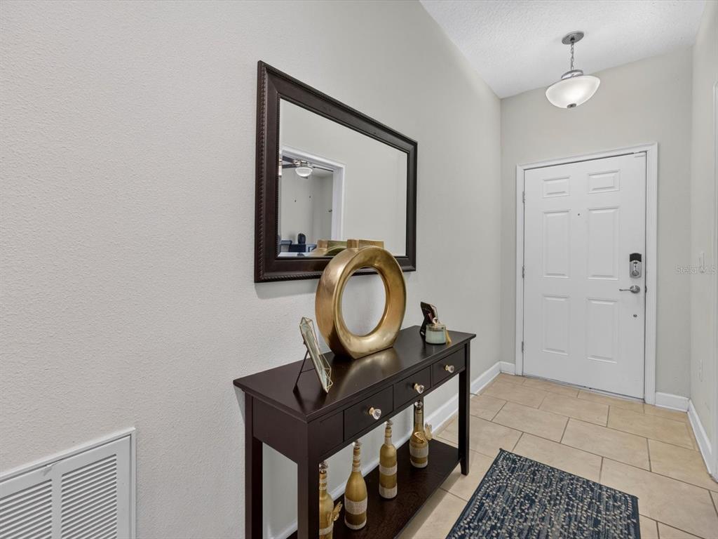 An entryway features a dark wood console table, a wall mirror, and a white front door — 3530 FAIRWATERS COURT UNIT D, CLERMONT, FL