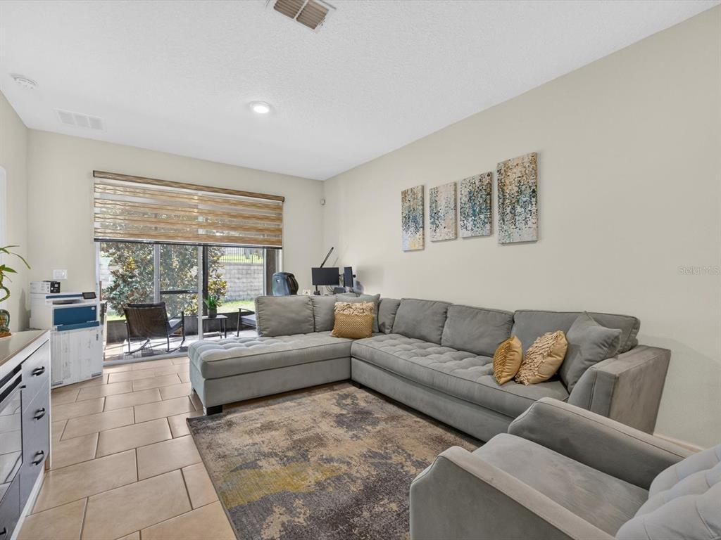 A living room features a large gray sectional sofa, a patterned area rug, and tile flooring — 3530 FAIRWATERS COURT UNIT D, CLERMONT, FL