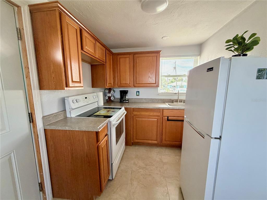 A kitchen with wood cabinets, white appliances, a window, and light-colored tile flooring — 233 WILLIAMS AVENUE, DAYTONA BEACH, FL