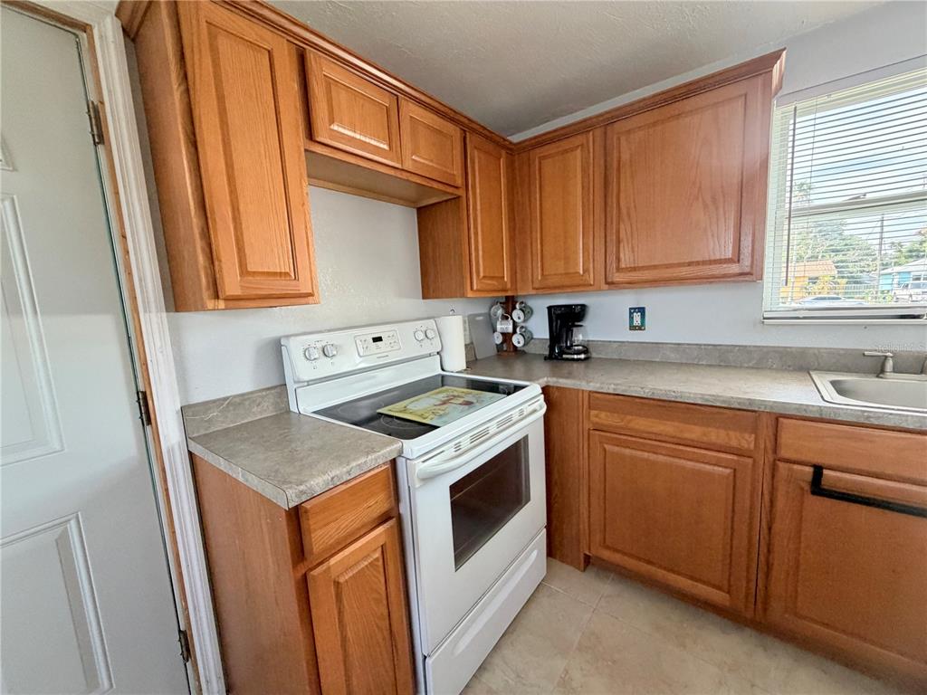 A kitchen features wood cabinets, a white electric stove, and laminate countertops — 233 WILLIAMS AVENUE, DAYTONA BEACH, FL