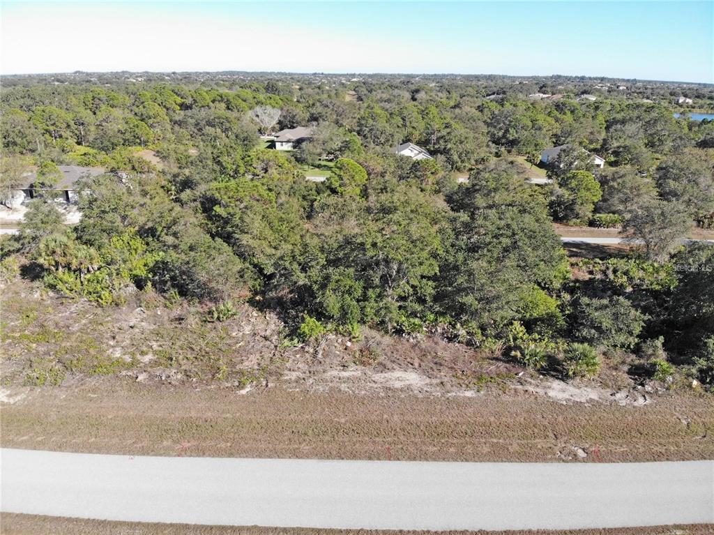 An aerial view shows a vacant, wooded residential lot adjacent to a paved road — 10080 WINBOROUGH DRIVE, PORT CHARLOTTE, FL