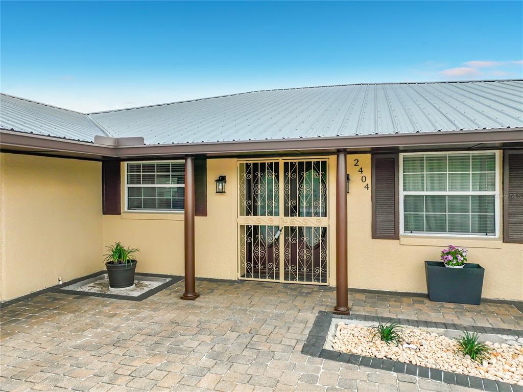 The exterior of a house features a paved patio, a metal roof, and a screen door — 2404 LAUDERDALE COURT, ORLANDO, FL