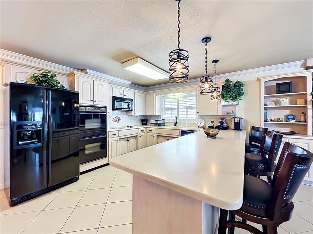 A kitchen features white cabinets, black appliances, a large island with seating, and pendant lighting — 2404 LAUDERDALE COURT, ORLANDO, FL