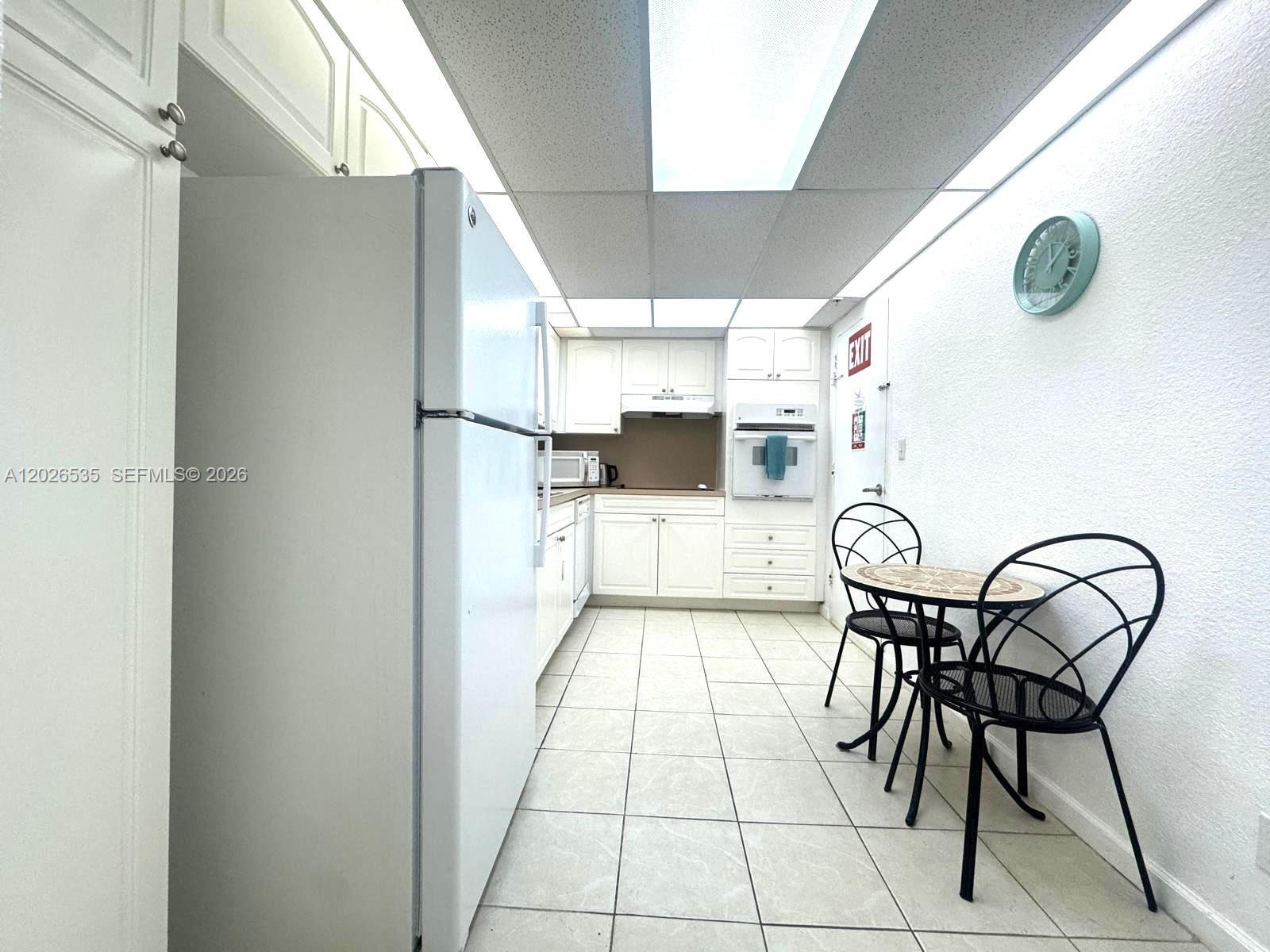A kitchen features white cabinets, a refrigerator, tile flooring, and a small dining set — 4001 S Ocean Dr # 15L, Hollywood FL 33019, HOLLYWOOD, FL