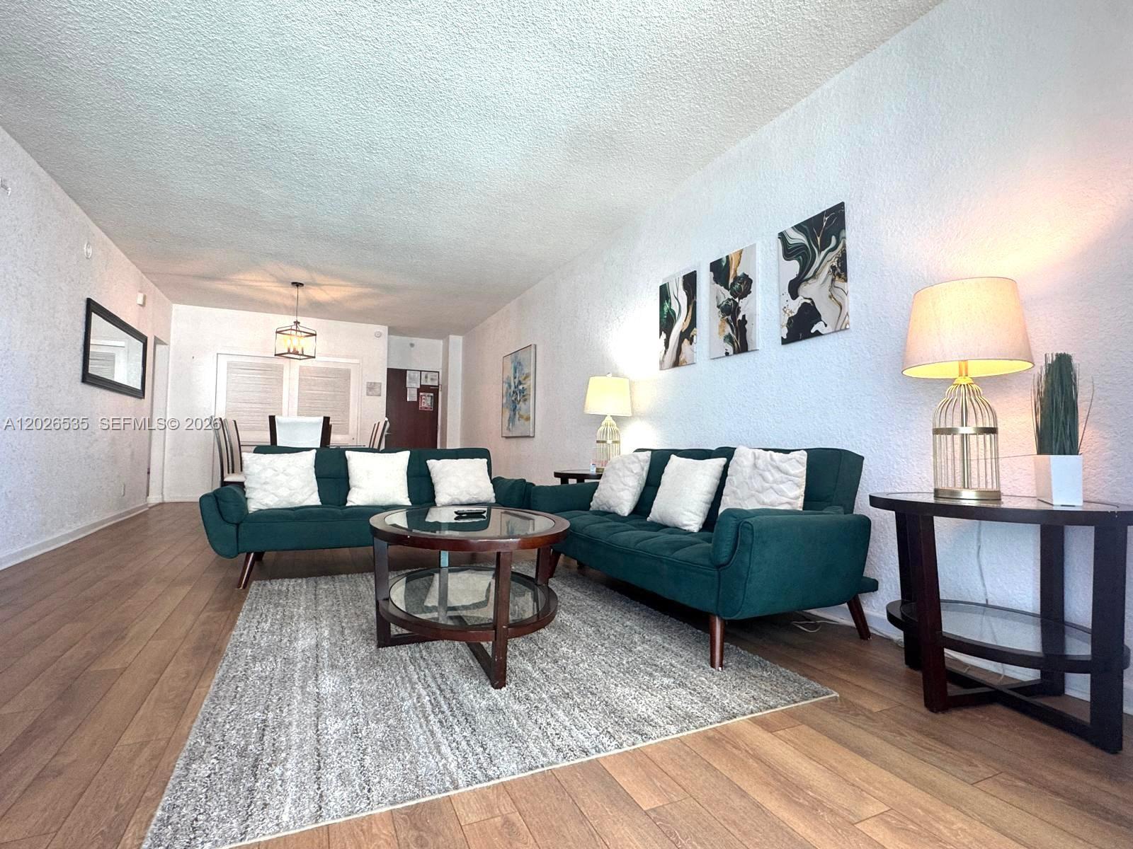 A living room features two dark green sofas, a glass coffee table, and wood flooring — 4001 S Ocean Dr # 15L, Hollywood FL 33019, HOLLYWOOD, FL