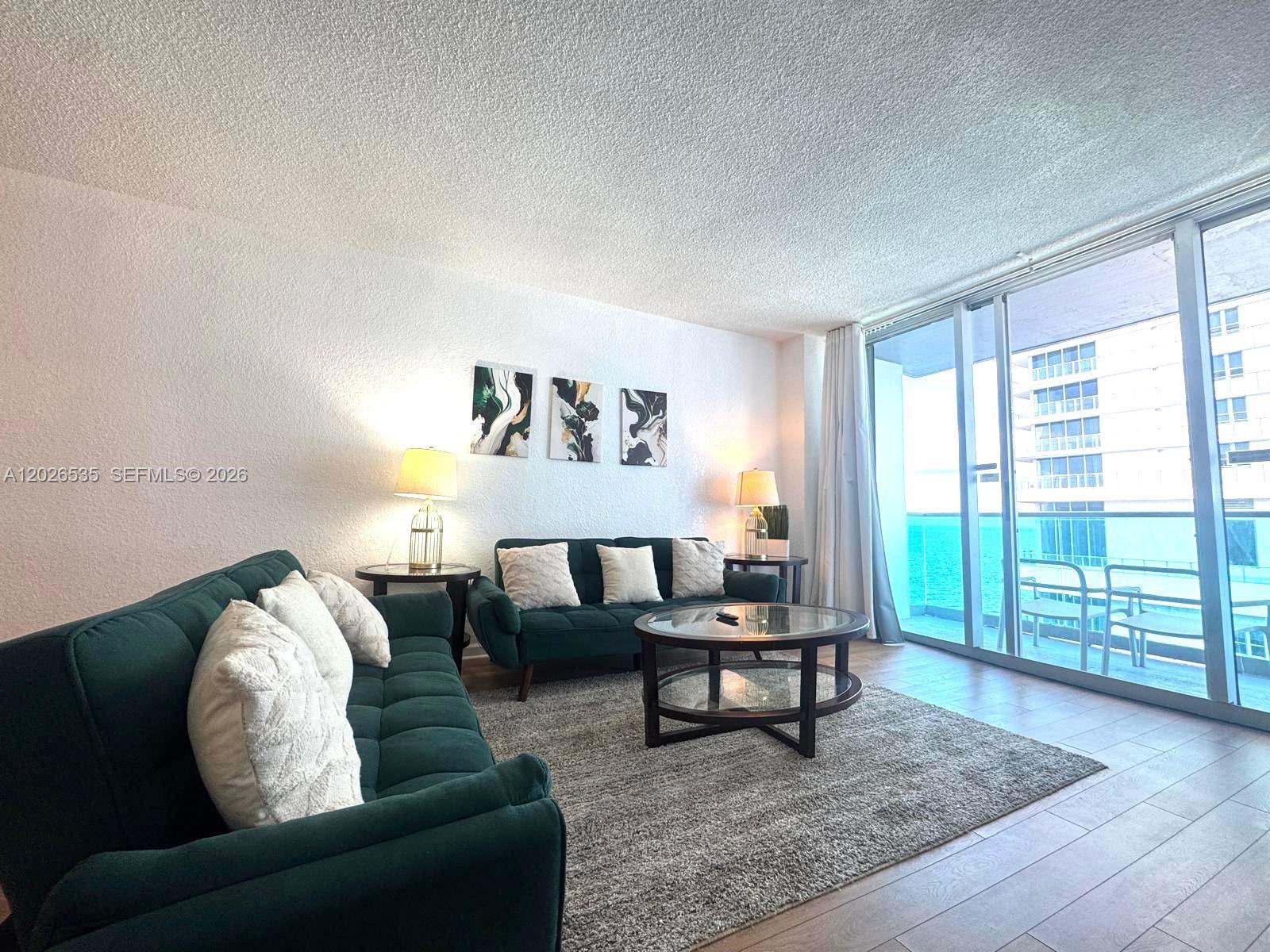 A living room features two dark green sofas, a glass coffee table, and a balcony view — 4001 S Ocean Dr # 15L, Hollywood FL 33019, HOLLYWOOD, FL