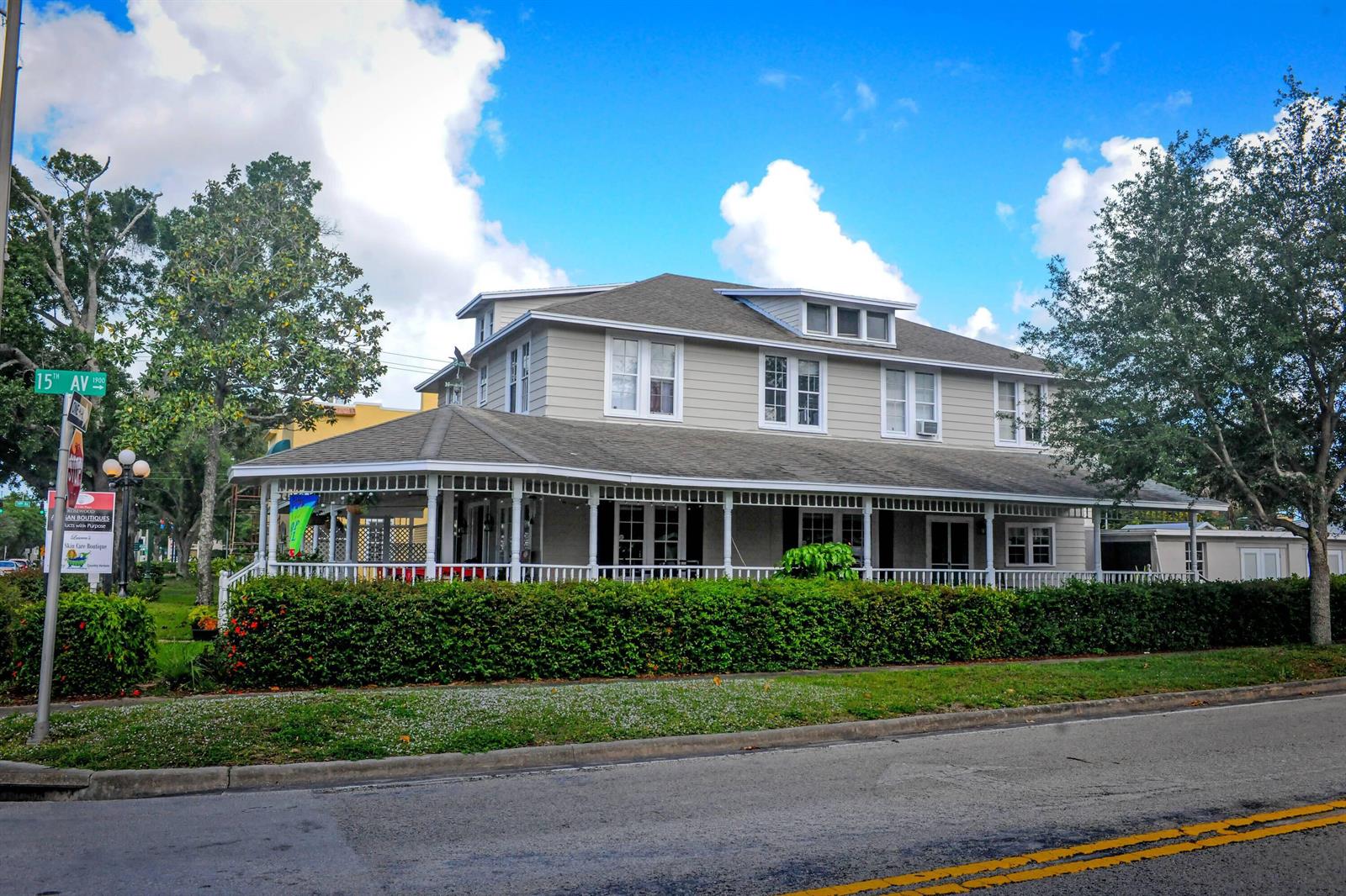 A two-story house with light gray siding and a wrap-around porch behind a green hedge — 1443 19th Place, Vero Beach FL 32960, VERO BEACH, FL