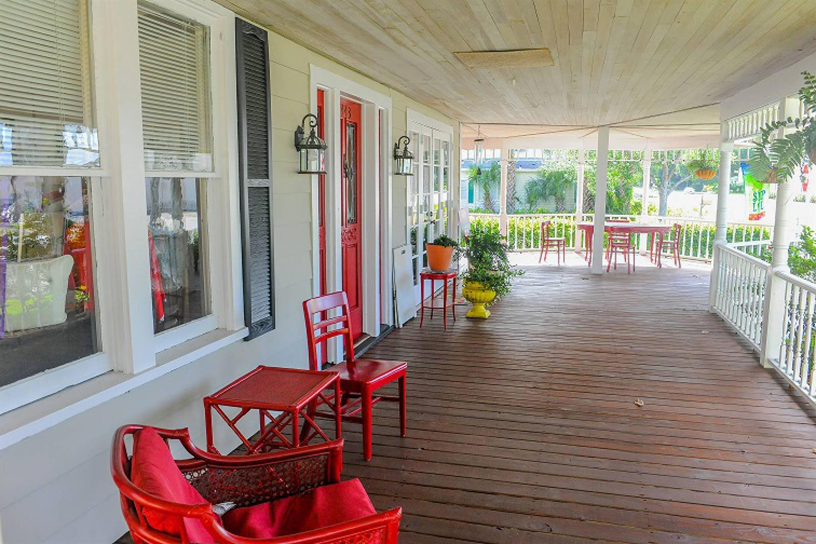 A wide wooden porch features red furniture, a red front door, and white railings — 1443 19th Place, Vero Beach FL 32960, VERO BEACH, FL