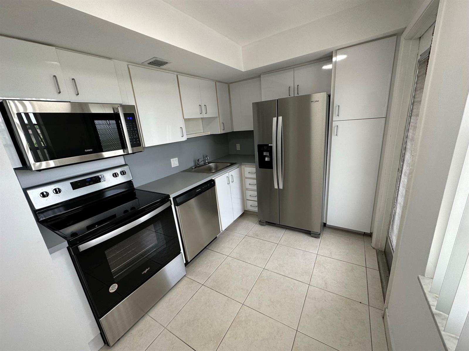 A kitchen features white cabinets, stainless steel appliances, gray countertops, and light-colored tile flooring — 2651 S Course Drive # 503, Pompano Beach FL 33069, POMPANO BEACH, FL