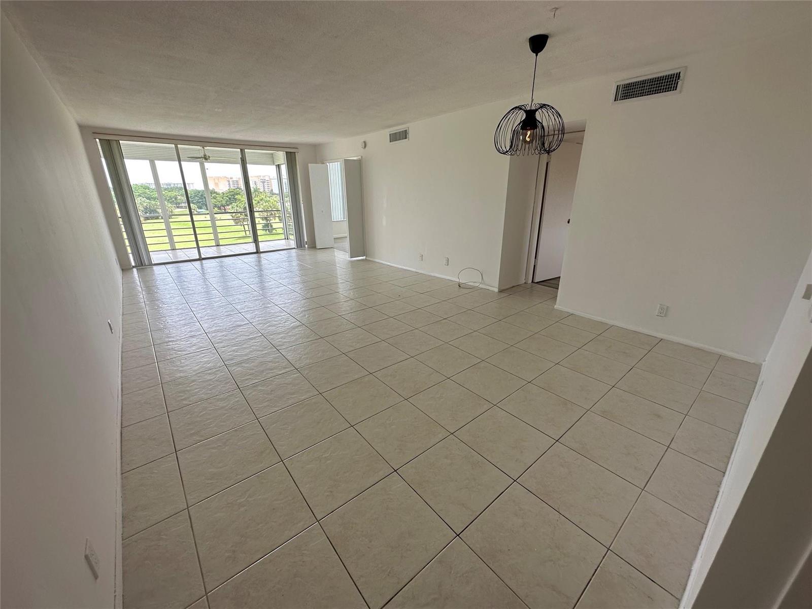 An empty living room features large beige floor tiles, white walls, and a sliding glass door — 2651 S Course Drive # 503, Pompano Beach FL 33069, POMPANO BEACH, FL