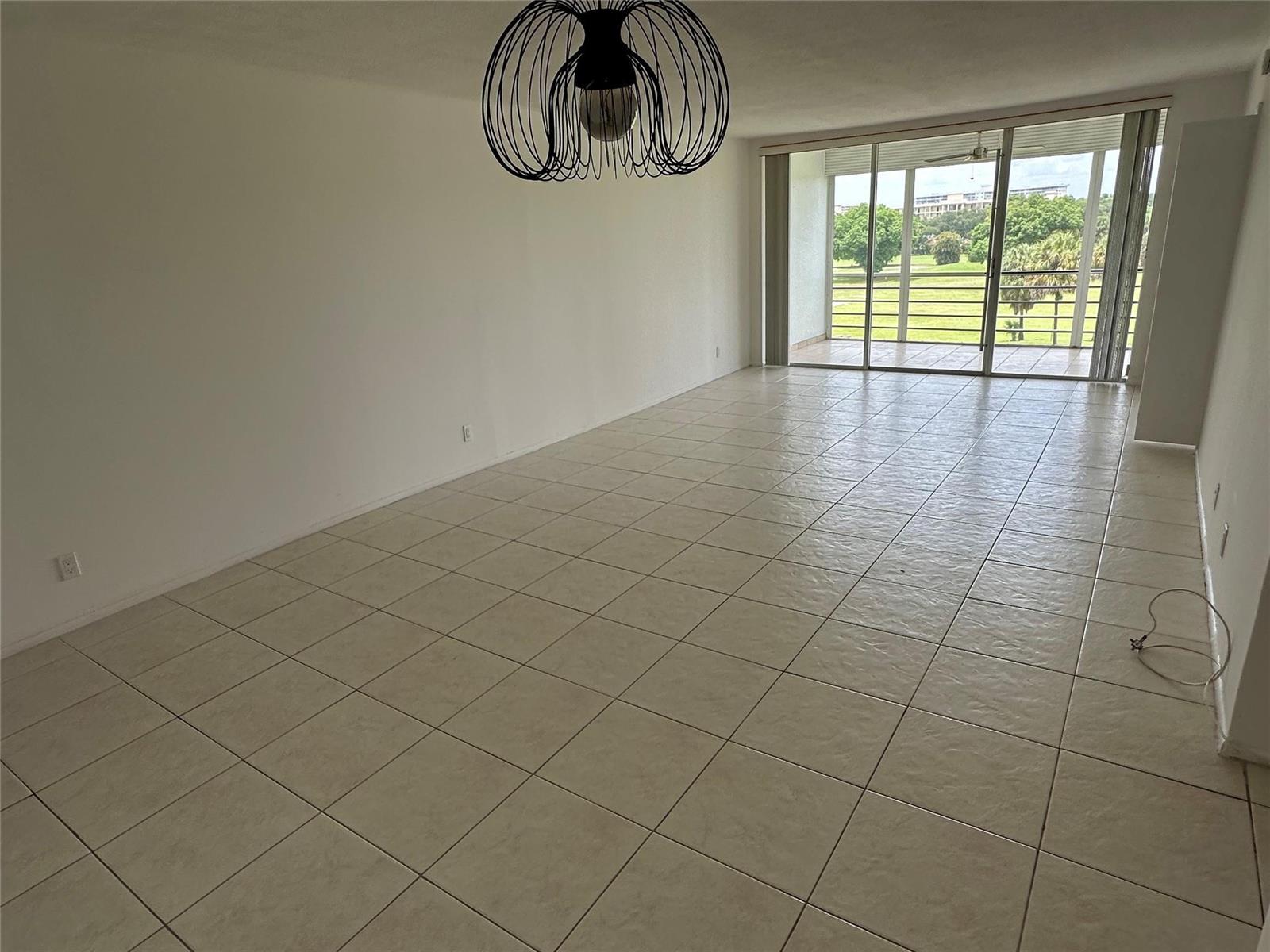 An empty room with light tile flooring, a wire pendant light, and a sliding glass door — 2651 S Course Drive # 503, Pompano Beach FL 33069, POMPANO BEACH, FL