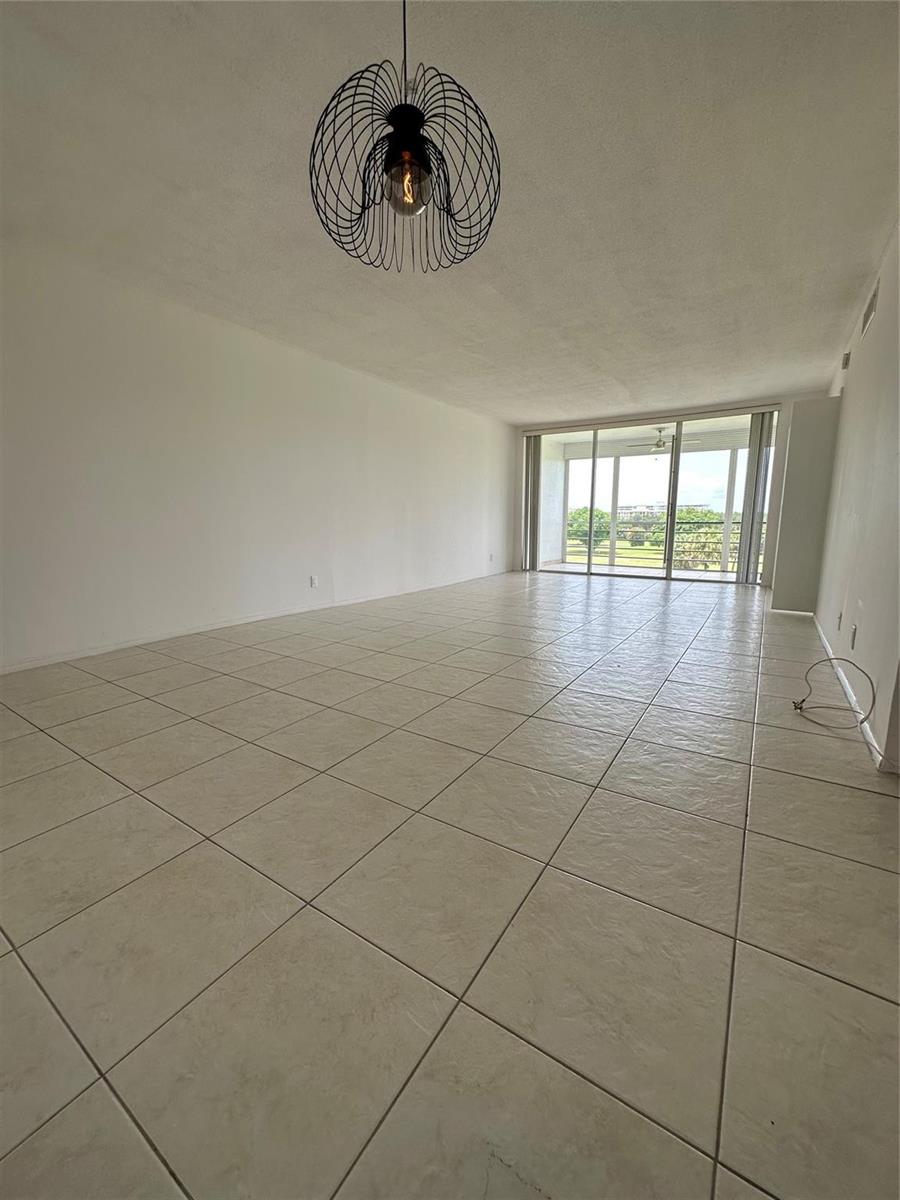 An empty living room with light tile flooring, a modern wire pendant light, and balcony access — 2651 S Course Drive # 503, Pompano Beach FL 33069, POMPANO BEACH, FL