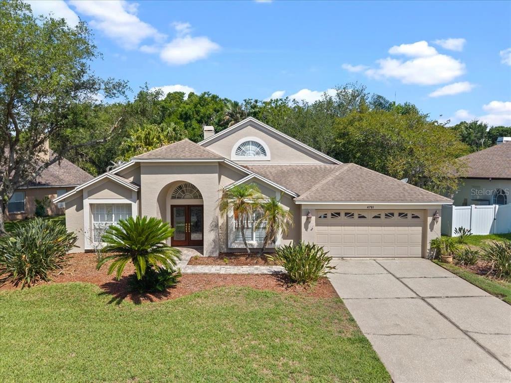 A beige single-story house with a two-car garage, arched entryway, and a landscaped front yard — 4761 STONEBRIAR DRIVE, OLDSMAR, FL