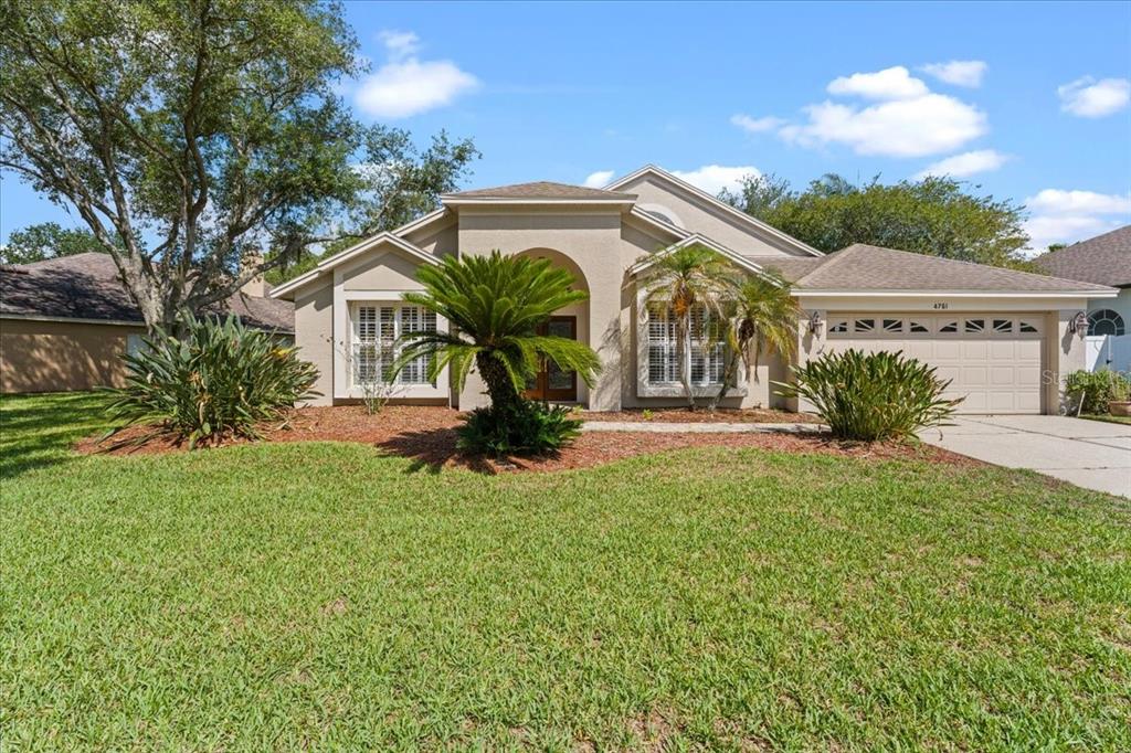 A single-story suburban house with a tan stucco exterior, a two-car garage, and landscaping — 4761 STONEBRIAR DRIVE, OLDSMAR, FL
