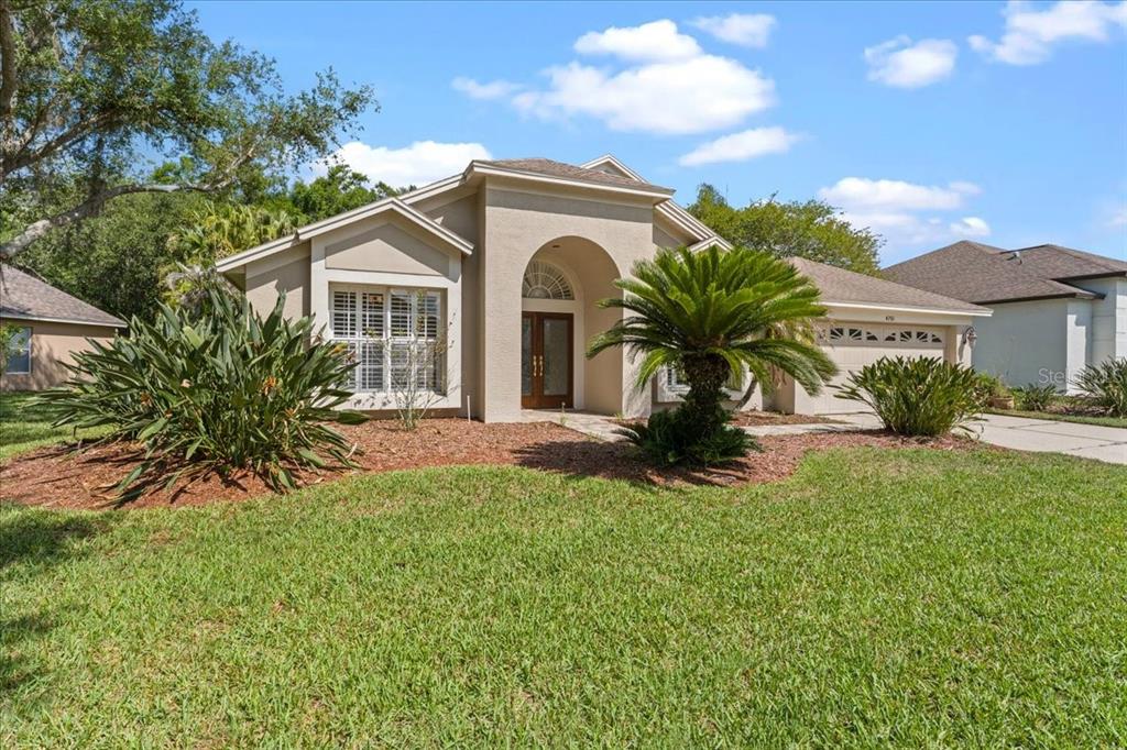 A single-story beige house with a arched entryway, a palm tree, and a grassy lawn — 4761 STONEBRIAR DRIVE, OLDSMAR, FL