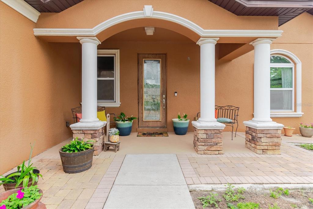A covered front porch features stone-based columns, a glass-paneled door, and potted plants — 2603 BISMARK DRIVE, VALRICO, FL