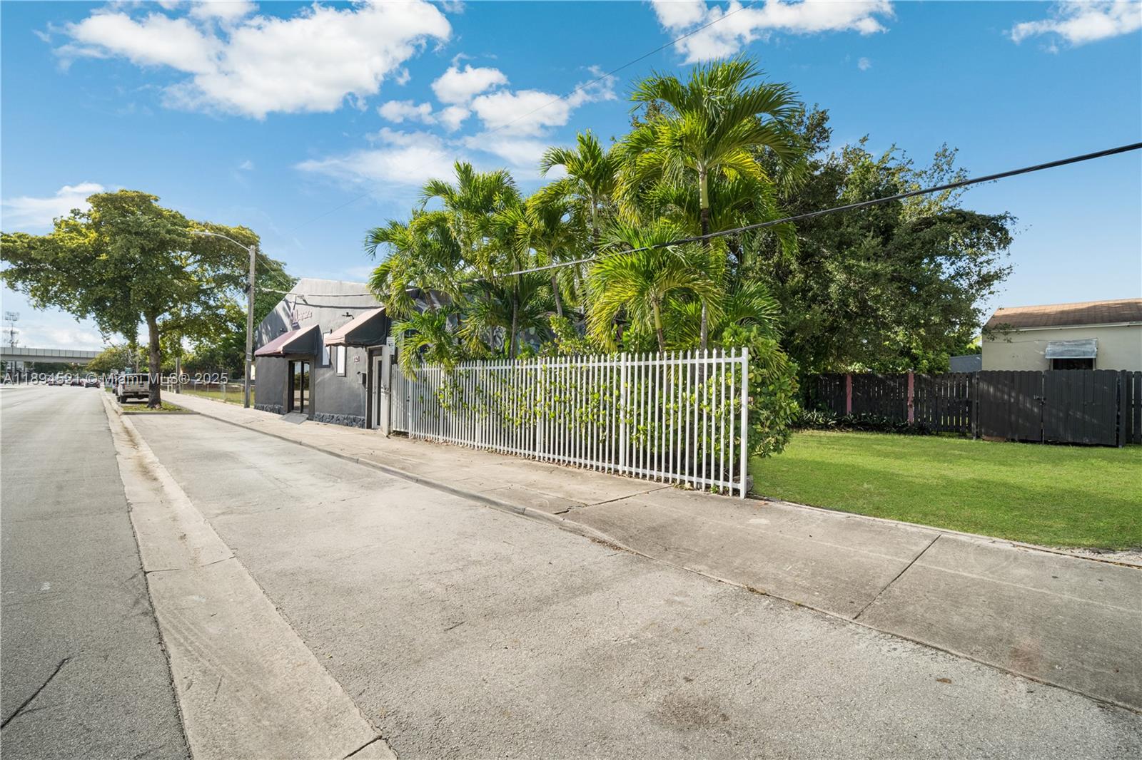 A gray commercial building sits behind a white metal fence next to palm trees — 1121 NW 29th St, Miami FL 33127, MIAMI, FL