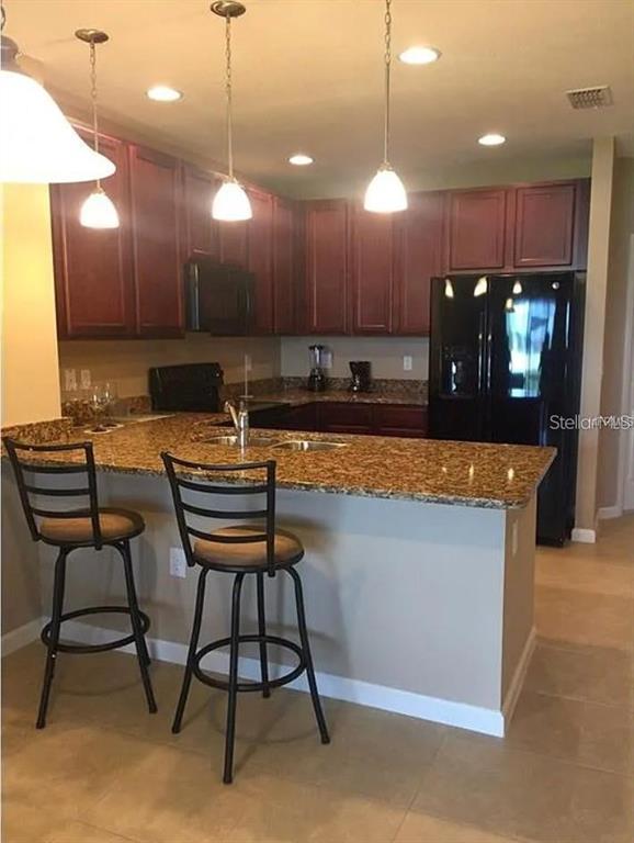A kitchen features dark wood cabinets, granite countertops, a breakfast bar, and black appliances — 1560 CHELSEA DRIVE, DAVENPORT, FL