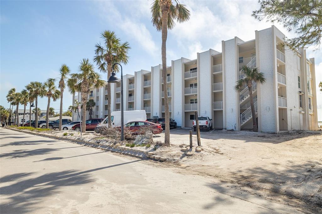 A multi-story white apartment building with palm trees and parked cars in front — 200 1ST AVENUE UNIT 212, ST PETE BEACH, FL