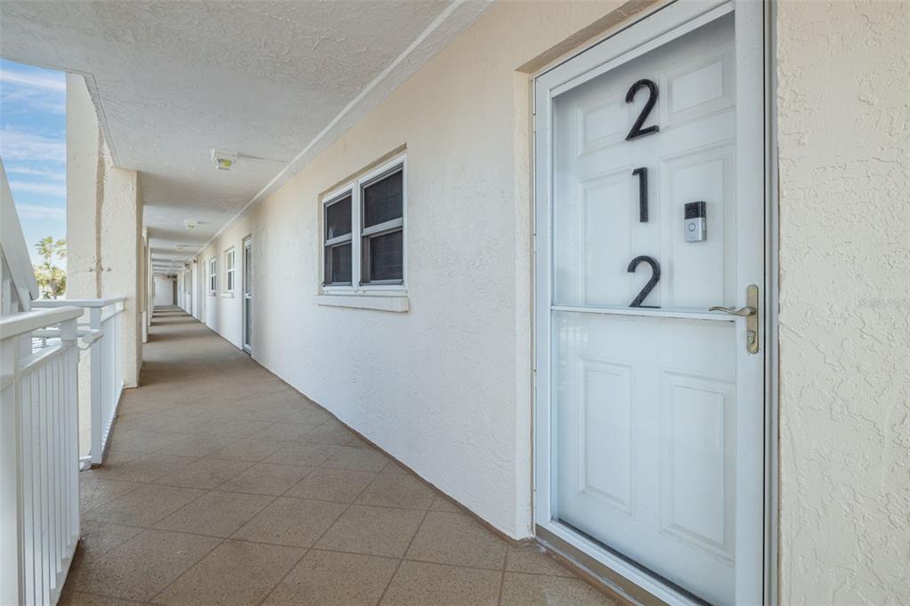 An exterior view of an apartment building walkway with a white door labeled 212 — 200 1ST AVENUE UNIT 212, ST PETE BEACH, FL