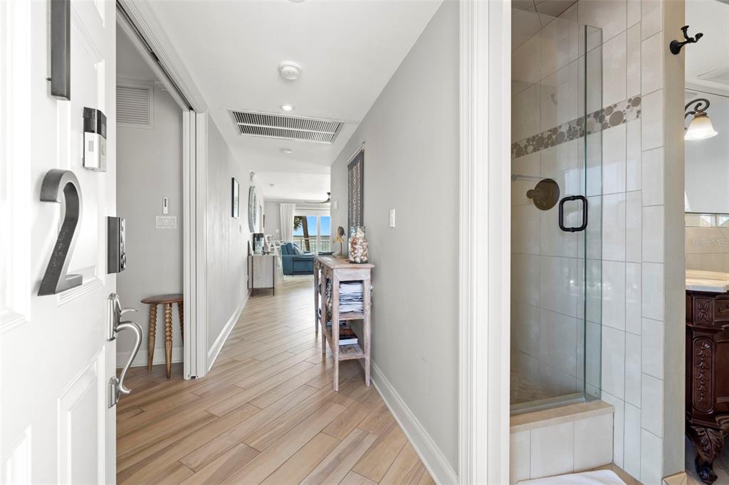 A hallway with wood-look flooring leads to a living area past a tiled glass shower — 200 1ST AVENUE UNIT 212, ST PETE BEACH, FL