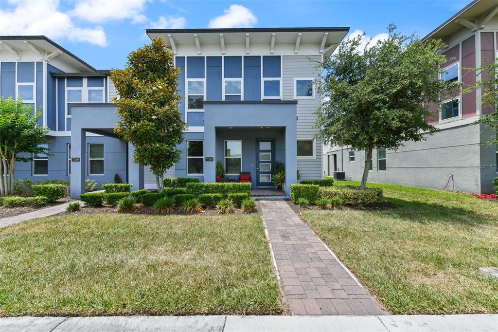 A modern two-story townhouse with blue siding, a flat roof, and a paved walkway — 7043 CARRICKBEND LANE, ORLANDO, FL